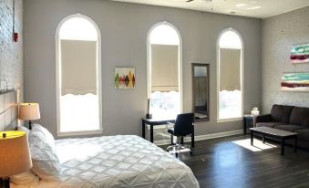 a modern bedroom with arched windows , wooden flooring , and a white bed , along with other furniture at Cornerstone Inn