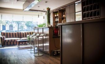 a modern bar with wooden floors , a long counter , and various chairs and stools surrounding it at Hotel Carlton