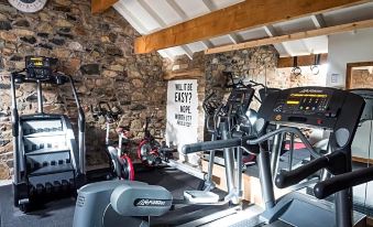 a gym with various exercise equipment , including treadmills and stationary bikes , is shown in front of a stone wall at The Wayside and Whisky Barn