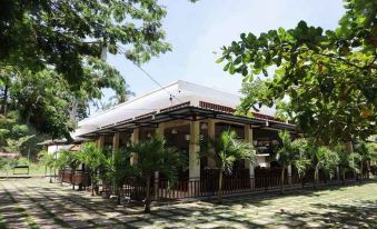 a traditional asian building with a red roof and white walls , surrounded by lush green trees and a clear blue sky at Hotel Grand Papua Kaimana