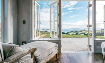 a bedroom with two doors that open , revealing a view of the ocean and mountains outside at Mudbrick Cottages