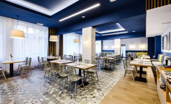 a modern dining room with wooden floors , blue walls , and white tables and chairs , creating an elegant atmosphere at Best Western Hotel Jurata
