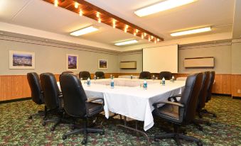 a conference room with a round table surrounded by black chairs and white tablecloth , surrounded by wooden walls and ceiling lights at Best Western Plus Longbranch Hotel  Convention Center