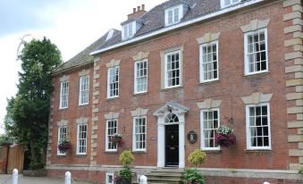 a large , red brick house with white trim and multiple windows , situated in a courtyard surrounded by trees at Colton House