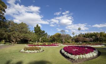 a large park with a variety of colorful flowers , including red and white ones , surrounded by green grass at The Wellington Apartment Hotel