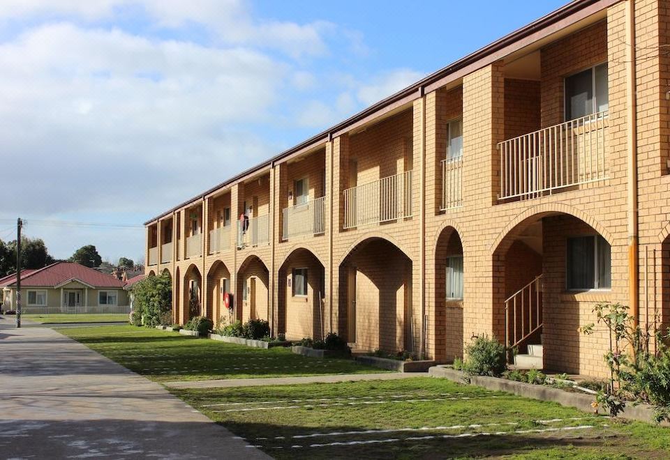 a brick building with multiple balconies and an arched walkway , under a blue sky with clouds at Colac Mid City Motor Inn