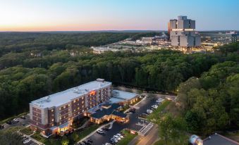 an aerial view of a large hotel surrounded by trees , with a parking lot in front of it at Hilton Garden Inn Stony Brook