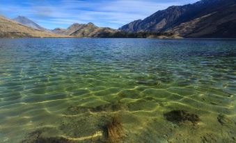 a serene mountain lake surrounded by green grass and mountains , with clear blue water reflecting the sky at Rosewood Matakauri