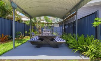 a modern outdoor space with a wooden table and bench , surrounded by greenery and blue fences at Tin Can Bay's Sleepy Lagoon Motel