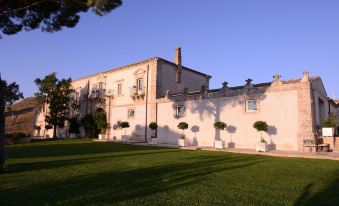 a large white building with a courtyard in front of it , surrounded by grass and trees at Castello Camemi