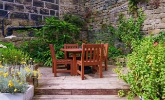 a wooden dining table and chairs set up on a patio , surrounded by lush greenery at Cross Keys