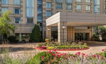 a modern hotel with a large entrance , surrounded by lush greenery and colorful flowers , under a clear blue sky at Sheraton Suites Chicago Elk Grove