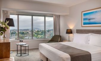 a hotel room with a large window , a bed , and a chair , providing a view of the city at Rydges Rotorua, an EVT Hotel