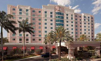 a large pink building with multiple stories and a red roof , surrounded by palm trees at DoubleTree by Hilton Sunrise - Sawgrass Mills