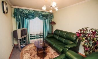 a living room with a green leather couch , coffee table , and curtains , along with a television in the corner at Norilsk