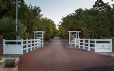 a white gate is open on a red walkway surrounded by trees and a fence at The Swan Valley Retreat