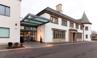 a modern building with a glass entrance , stone walls , and white walls , surrounded by trees and a clear sky at DoubleTree by Hilton London Heathrow Airport