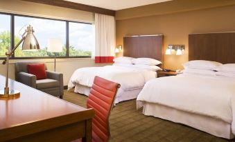 a hotel room with two beds , a desk , and a window , decorated with white bedding and red pillows at Four Points by Sheraton Winnipeg South