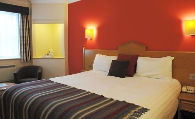 a hotel room with a red wall , a bed , and a lamp , along with a window and a desk at Village Hotel Liverpool