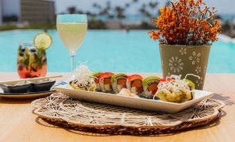 a dining table with a plate of sushi , a glass of wine , and a bowl of fruit at Radisson Blu Aruba
