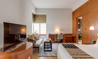 a hotel room with a king - sized bed , a flat - screen tv , a desk , and a couch at The Manor - New Delhi