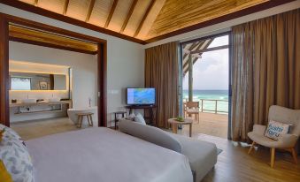 a bedroom with a bed and a television , overlooking the ocean through a large window at Fushifaru Maldives