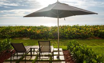 a patio area with two lounge chairs and an umbrella , surrounded by a lush green garden at DoubleTree Suites by Hilton Melbourne Beach Oceanfront