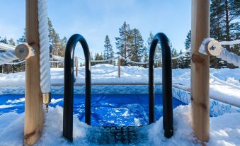 a hot tub covered in snow , surrounded by a wooden deck and trees in the background at Northern Lights Village