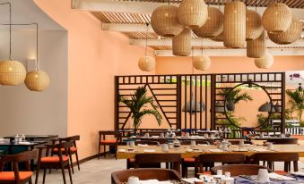 a restaurant with wooden tables and chairs , surrounded by potted plants and hanging lights , set against an orange wall at Salt of Palmar, Mauritius