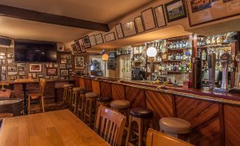 a bar with wooden stools and a long counter filled with bottles , framed pictures on the wall at Sandhouse Hotel