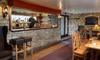 a bar with a stone wall , wooden tables and chairs , and a bartender behind the counter at Best Western the Compass Inn