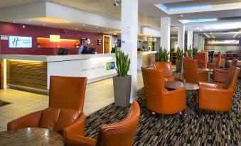 a modern hotel lobby with orange leather chairs and couches , a reception desk , and potted plants at Holiday Inn Express Stevenage