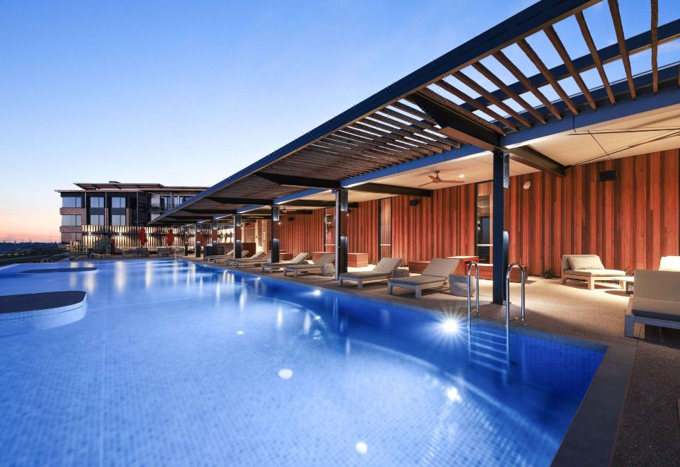 a large swimming pool with a wooden structure and lounge chairs is shown in the image at The Sebel Yarrawonga Silverwoods