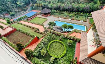 a lush green garden with a pool and a house in the background , surrounded by trees at DAM San Hotel