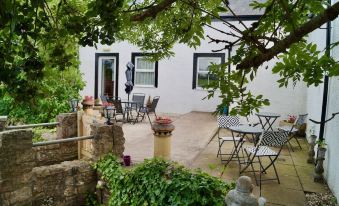 a patio with a stone wall , white building , and several tables and chairs in the background at Old Posting House