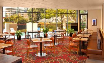 a restaurant with wooden tables and chairs , large windows , and a red carpet , offering a view of a swimming pool outside at Four Points by Sheraton - San Francisco Bay Bridge