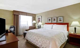 a large bed with white linens is in a room with a chair , desk , and window at Holiday Inn Laval - Montreal