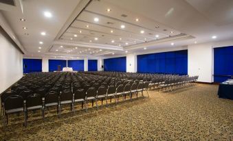a large , empty auditorium with rows of black chairs and blue curtains , set against a white ceiling with exposed lights at Hotel Dann Carlton Medellín