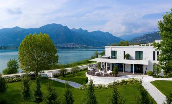 a large white house situated on the shore of a lake , surrounded by trees and mountains at Bianca Relais
