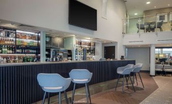 a modern bar with a blue countertop , multiple stools , and a tv mounted on the wall at DoubleTree by Hilton London Heathrow Airport