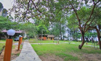 a lush green park with a paved walkway , trees , and a small building in the background at Baan Chao Mai Beach House