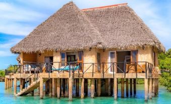 a wooden hut with a thatched roof is situated on stilts in the middle of the ocean at Chale Island Resort