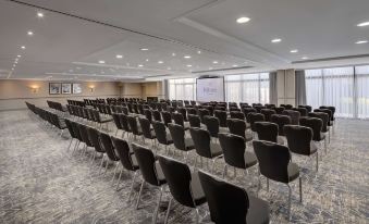 a large conference room with rows of chairs arranged in a semicircle , and a projector screen on the wall at Hilton Cobham