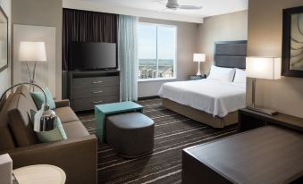 a modern hotel room with a large bed , couch , and flat screen tv , along with a view of the city through the window at Homewood Suites by Hilton Aliso Viejo Laguna Beach