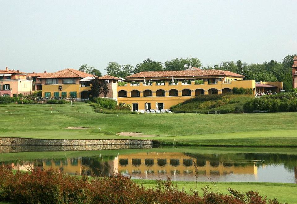 a large building with a red tile roof is surrounded by a green field and a pond at Doubletree by Hilton Milan Malpensa Solbiate Olona