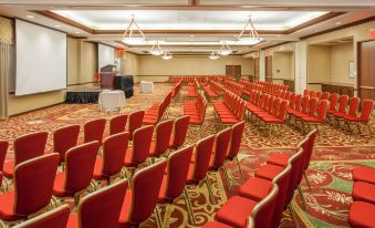 a large , empty conference room with rows of red chairs and a podium in the center at Sonesta Milwaukee West Wauwatosa