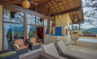 a luxurious hotel room with a large bed , couch , and a hot tub , surrounded by windows offering a view of the surrounding landscape at Sleeping Giant Rainforest Lodge