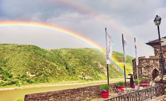 a rainbow arcs over a mountainous landscape , with flags and banners set up on a stone wall at Burg Reichenstein