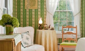 a cozy living room with green and white curtains , a wooden table , and a chair at The Waterford Inne