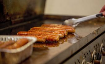 a close - up of hot dogs on a plate , with a spatula and some sausages in the background at Discovery Parks - Perth Airport